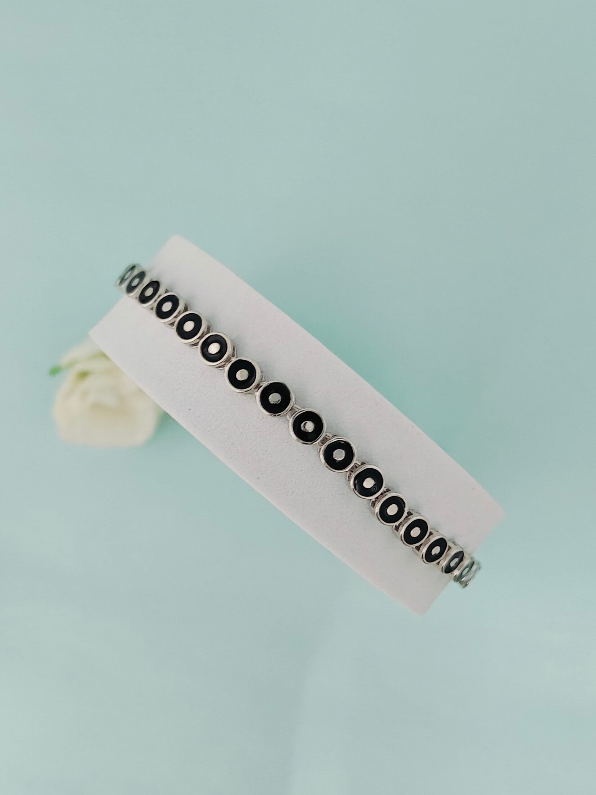 Silver bracelet with black stones on a white card against a light blue background